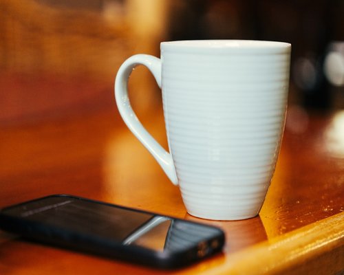 Mobile phone placed face down on a wooden table next to a coffee cup