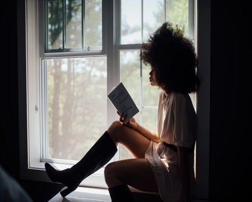 A person reading a physical book near a bright window